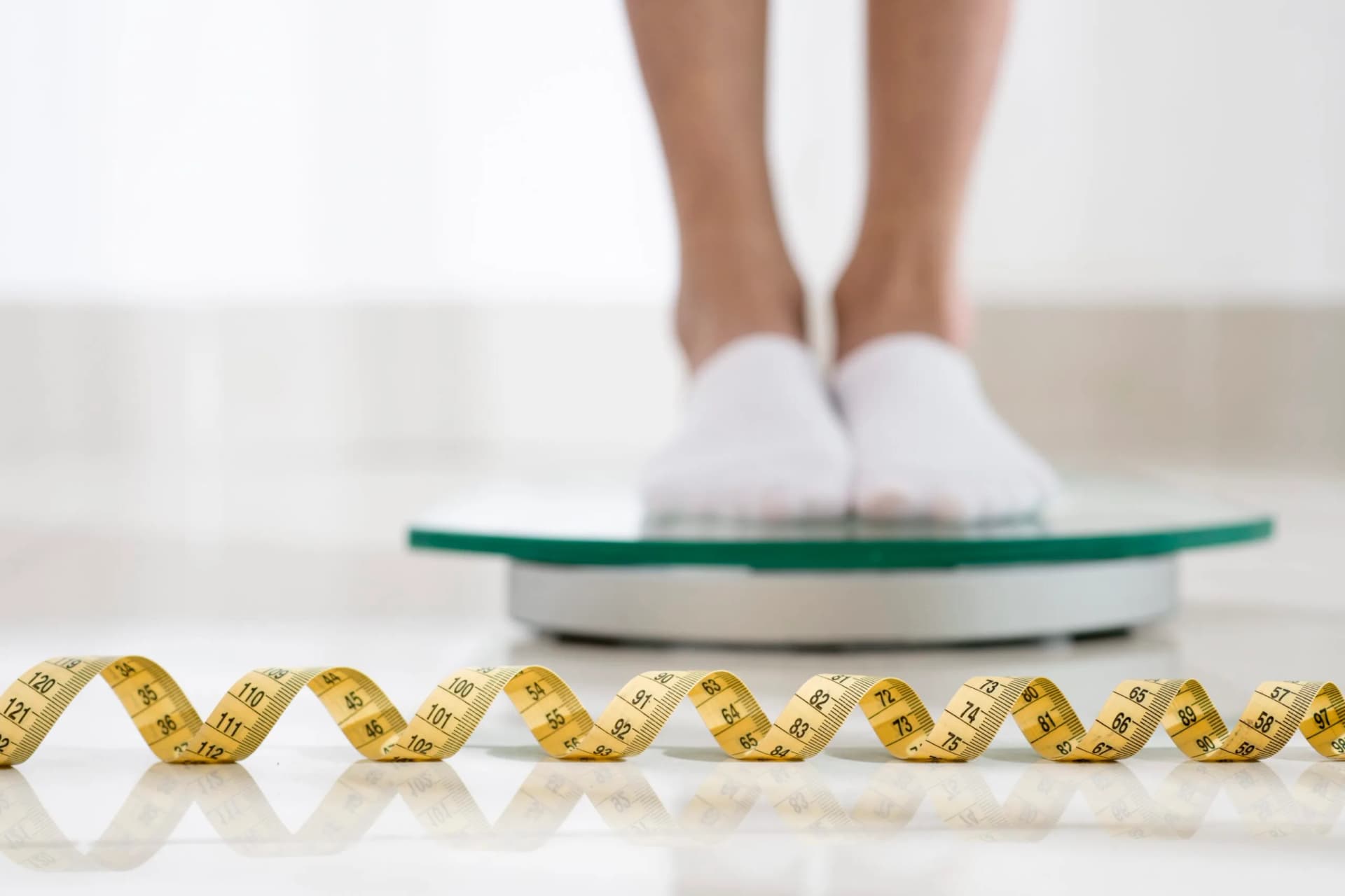 A person standing on bathroom scales with a tape measure on the floor