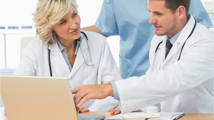 Two doctors review notes on a laptop together