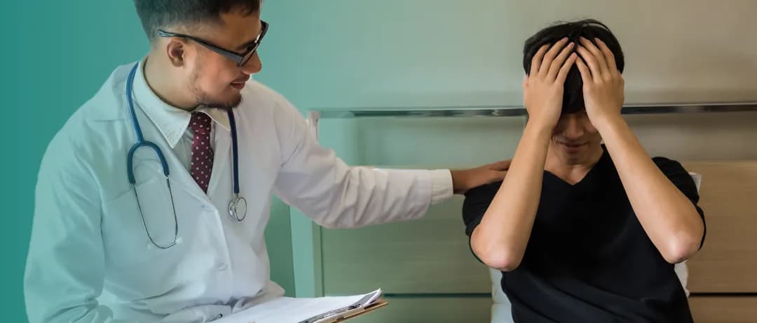 A doctor talks with a man holding his head in his hands