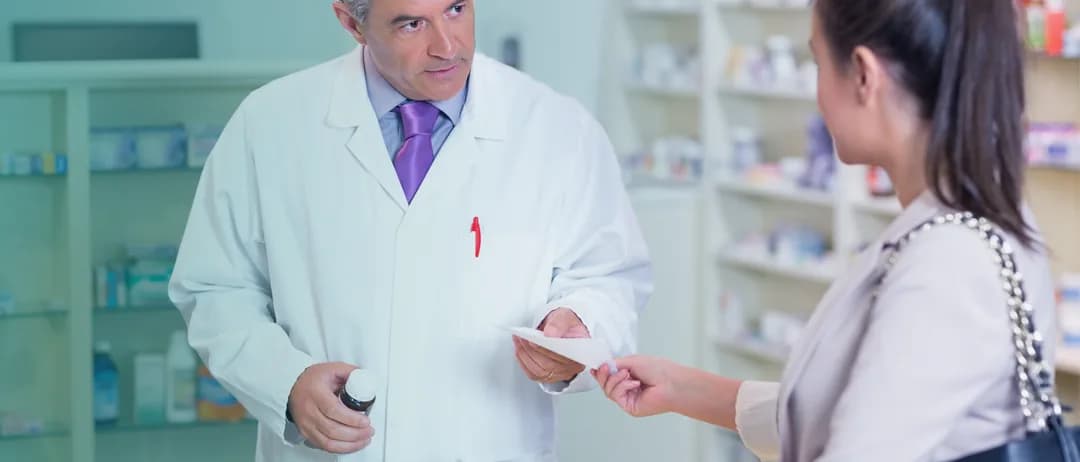 A pharmacist hands a prescription to a patient
