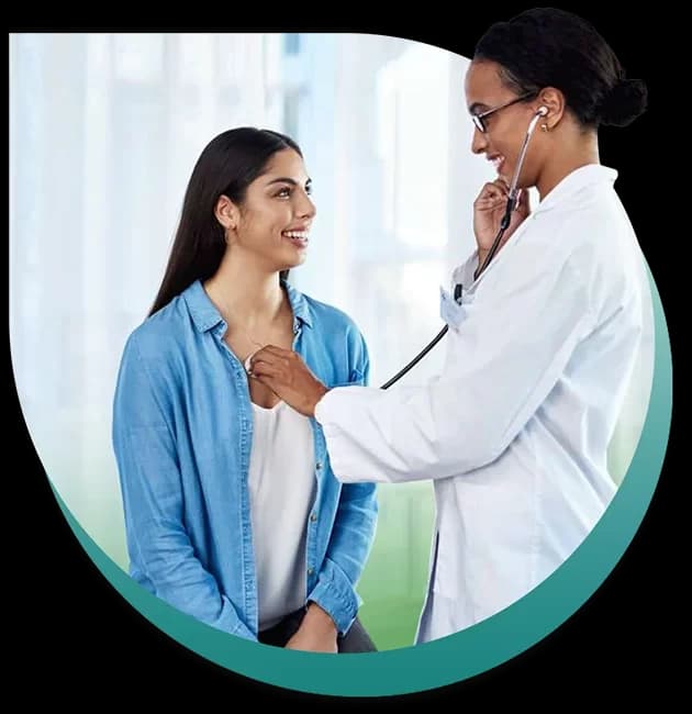 A doctor listens to a smiling patient’s chest with a stethoscope