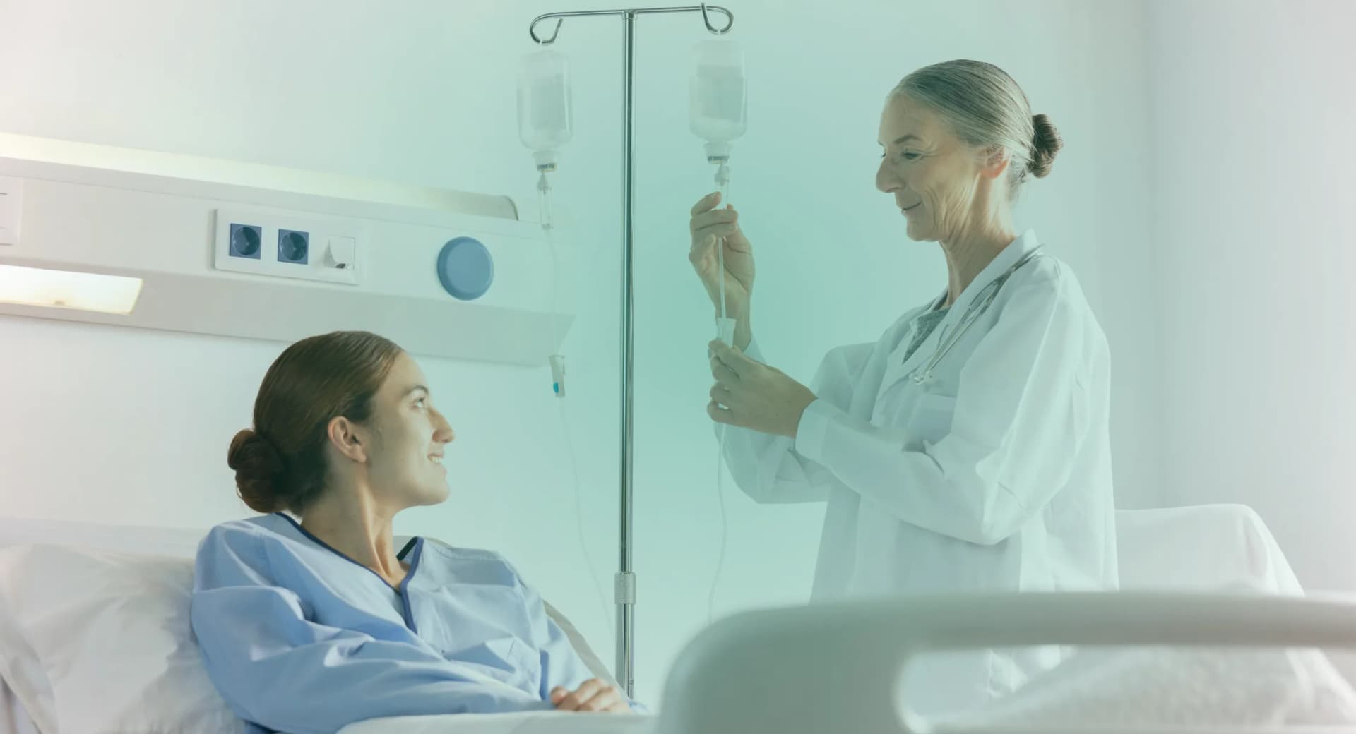 A nurse prepares an IV drip for a patient resting in a reclining bed